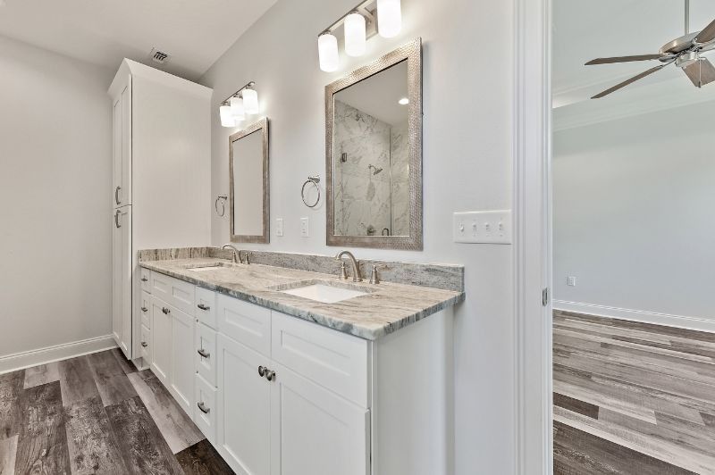 Bathroom with double vanity, white cabinets, granite countertop, large mirrors, and hardwood floors.