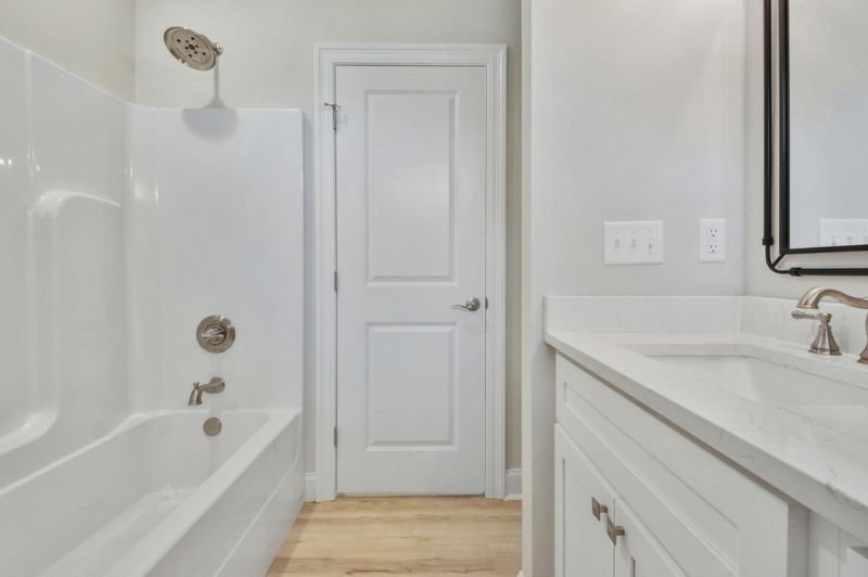 White bathroom with tub, vanity, and closed door.