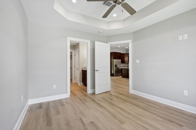 Empty bedroom with light gray walls, white trim, wood flooring, and doorways to other rooms.
