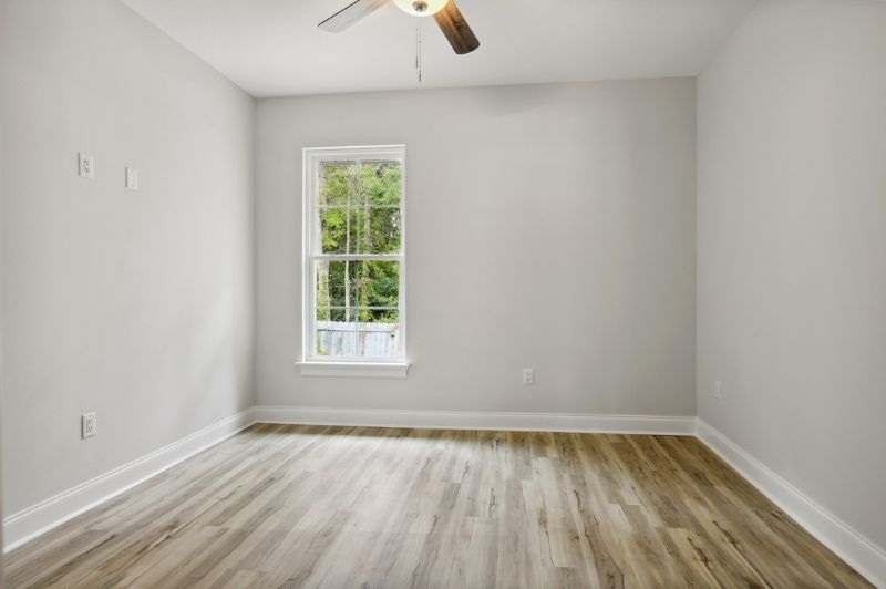 Empty bedroom with light wood floors, white walls, a window, and a ceiling fan.