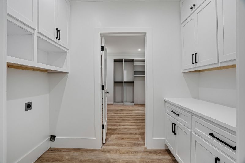 White laundry room with cabinets, open doorway to a closet.