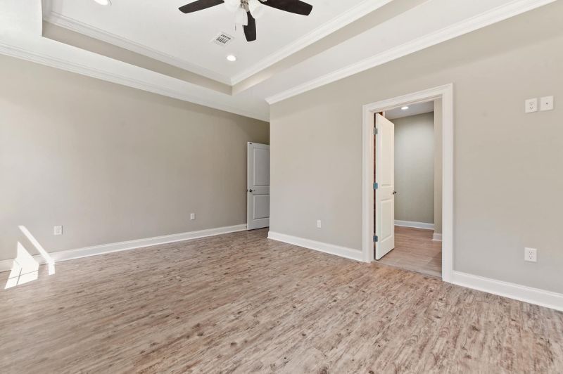 Empty bedroom with light brown wood-look floor, gray walls, white trim, and a tray ceiling.