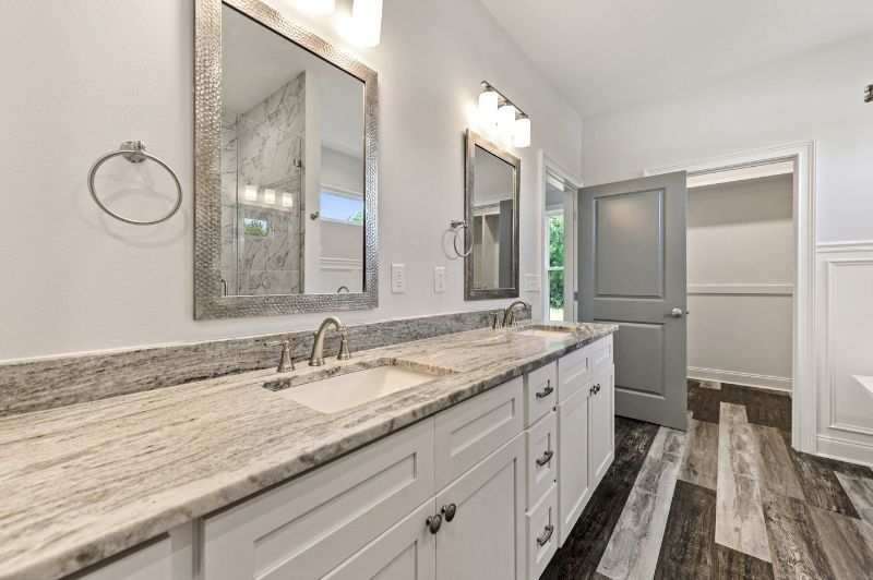 Bathroom with white vanity, granite countertop, two mirrors, and grey door.