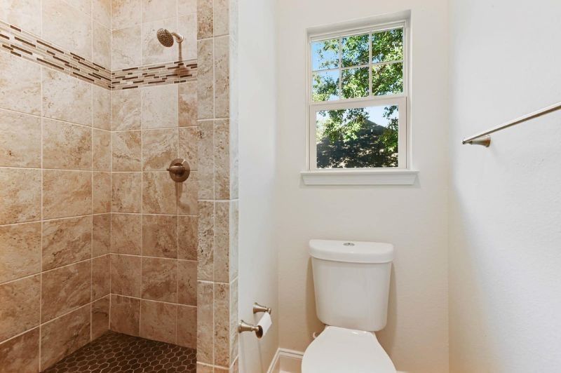 Bathroom with tiled shower, toilet, window, and towel rack.