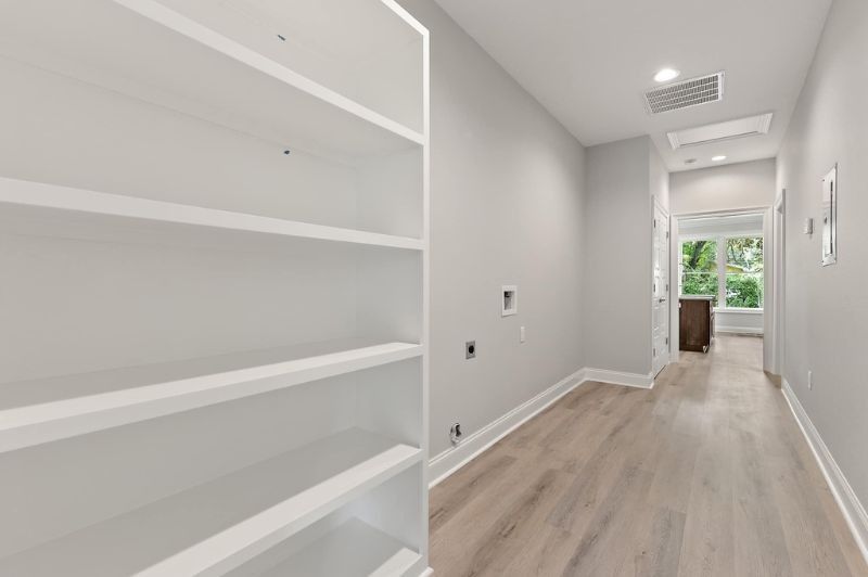 Empty hallway with white shelving, light wood floors, and gray walls.