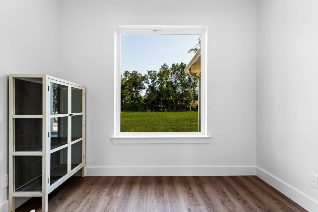 White room with window overlooking a green lawn, and a wooden cabinet on the left.