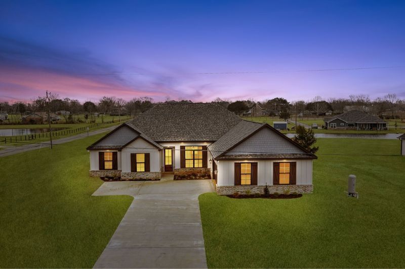 Ranch-style home with stone accents, brown shutters, and long driveway at dusk.