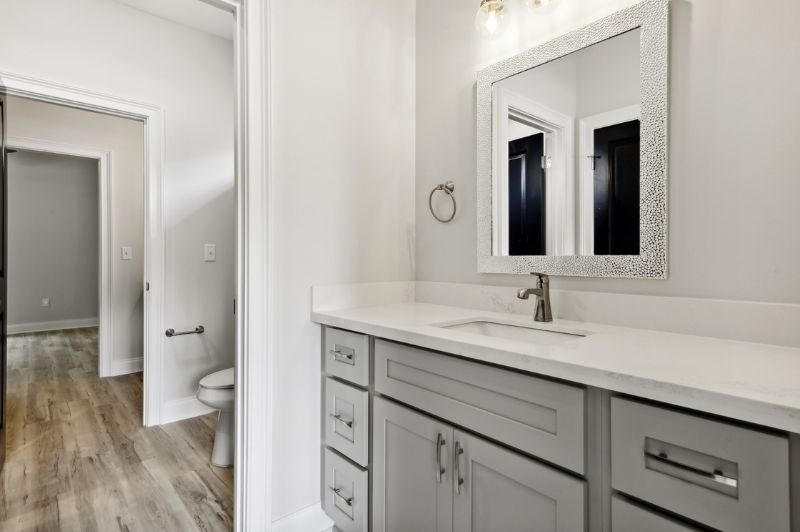 Bathroom with gray vanity, white countertop, silver faucet, and mirror. Doorway leads to toilet and hallway.