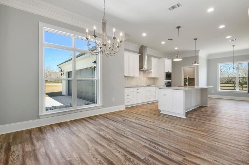 Spacious kitchen with white cabinets, island, and hardwood floors. Large windows offer natural light.