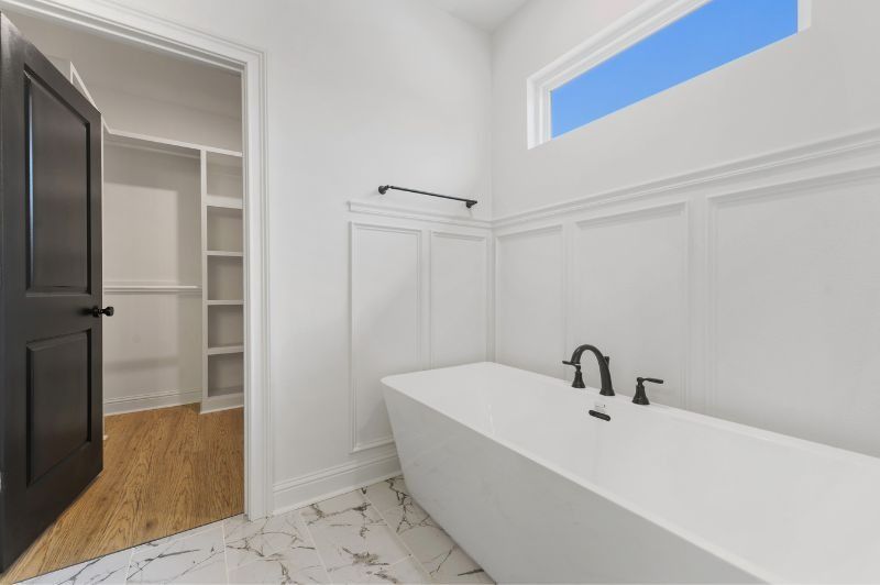Bathroom with white tub, walls, and window. Black door and faucet, closet visible.