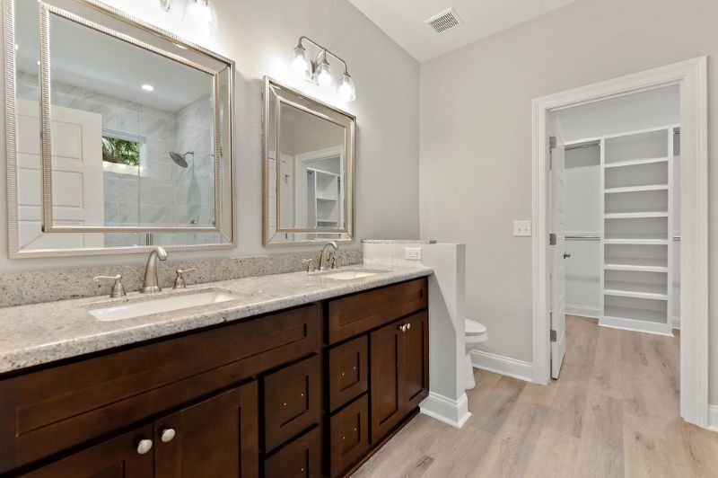 Bathroom with dark wood vanity, light-colored countertop, two mirrors, and a closet with white shelves.