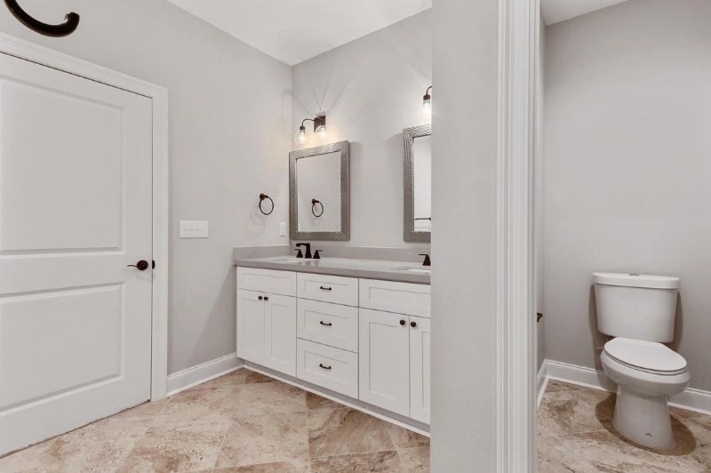 A modern bathroom with white cabinets, dual sinks, and a separate toilet area.