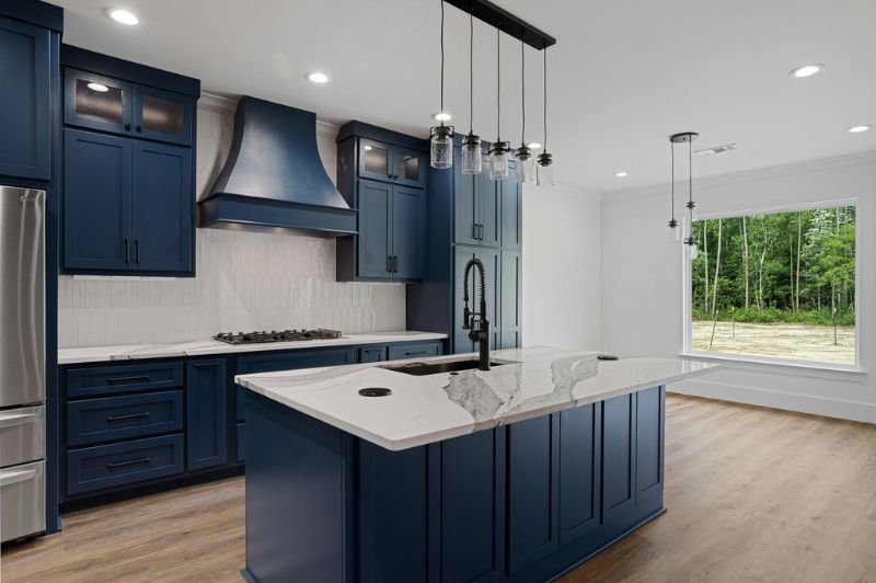 Navy blue kitchen with white countertops, island, and stainless steel appliances. Large window.