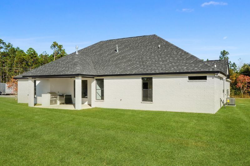 Back view of a white brick house with gray roof and green lawn under a blue sky.