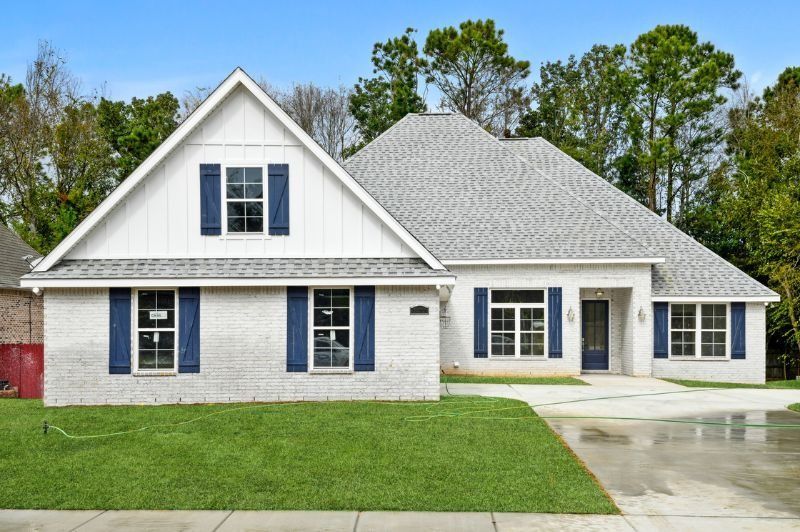 White brick house with blue shutters, gray roof, and green lawn.