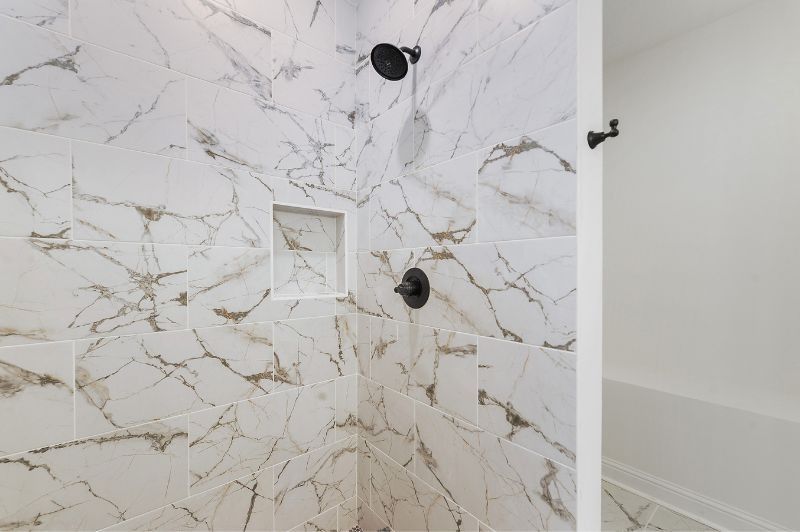 Shower with white marble-look tile and black fixtures, including shower head and faucet.