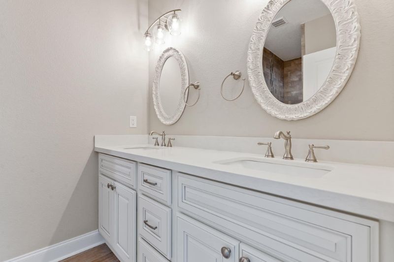 White double vanity bathroom with oval mirrors and brushed nickel fixtures.