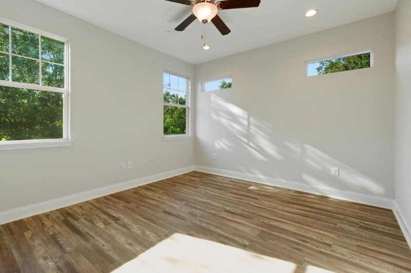 Empty room with wood floor, white walls, windows, and a ceiling fan.