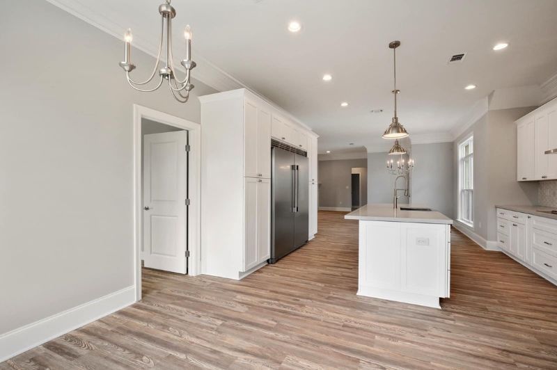 Open kitchen with white cabinets, island, and stainless steel refrigerator. Wood-look flooring and gray walls.