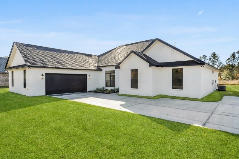 White house with black roof and garage, green lawn, clear sky.