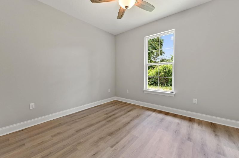 Empty bedroom with gray walls, wood-look floor, a window, and a ceiling fan.
