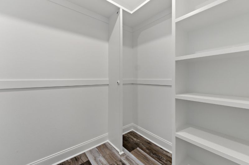 Empty, white closet with built-in shelves and wooden floorboards.  Door is partially open.