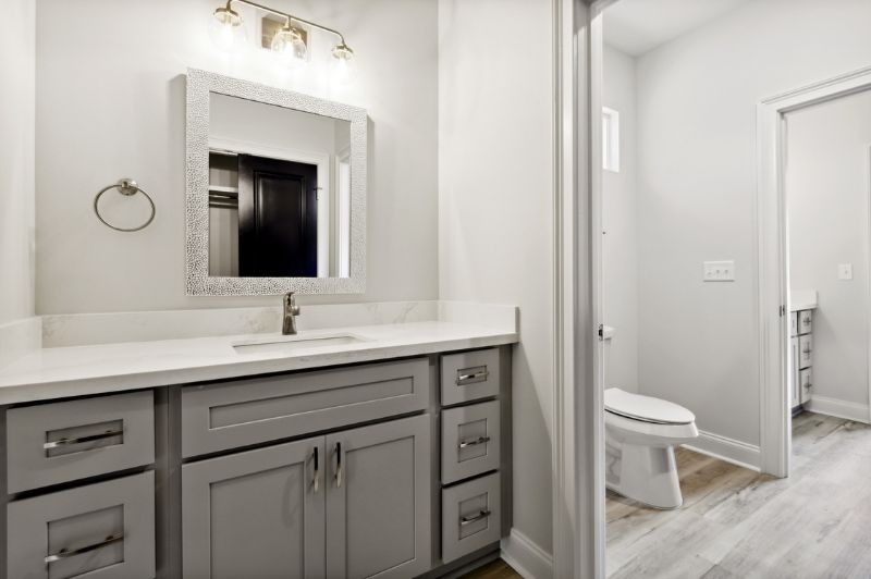 Bathroom with gray vanity, white countertop, square mirror, and door to toilet.