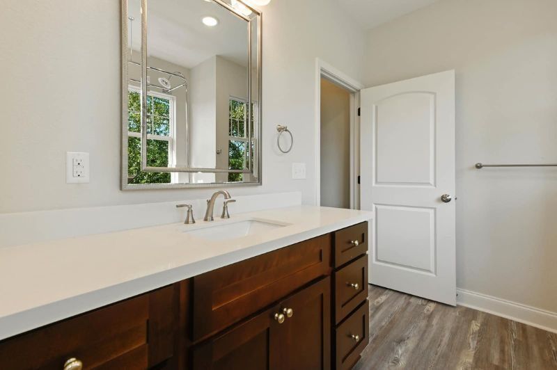 Bathroom with dark wood vanity, white countertop, silver mirror frame, and grey floor.