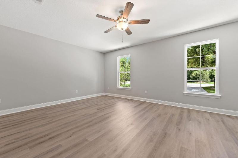 Empty room with gray walls, wood floors, two windows, and a ceiling fan.
