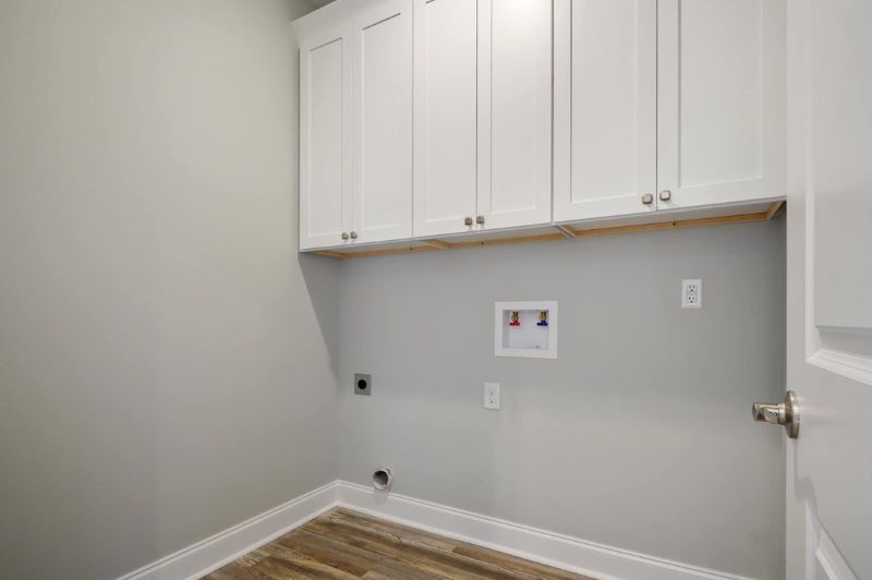Small, empty laundry room with white cabinets, gray walls, and wood-look flooring.