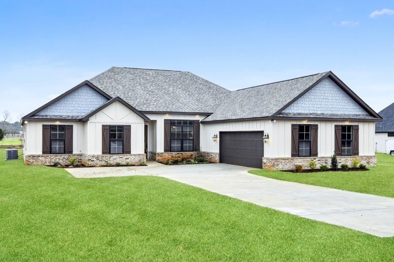 White house with gray roof and brown shutters, set on a green lawn, driveway in front.