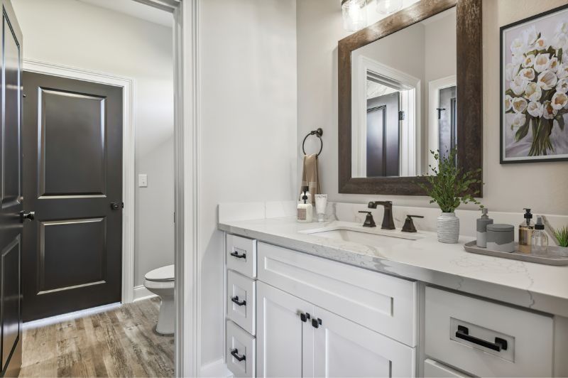 Bathroom with white vanity, marble countertop, dark mirror frame, dark door, and wooden floor.