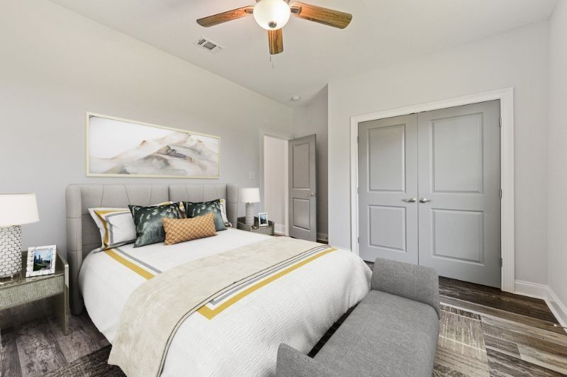 Bedroom with gray walls, bed with decorative pillows, artwork, and a bench at the foot of the bed.
