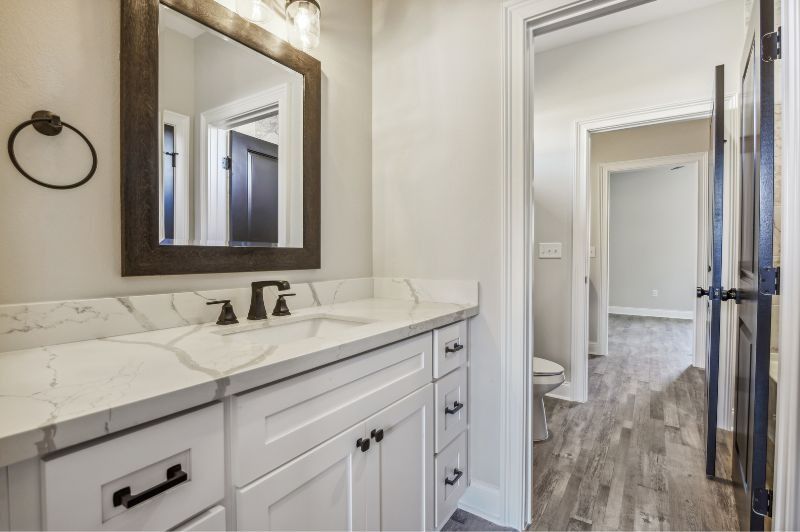 Bathroom with white vanity, marble countertop, dark accents, and doorway to hallway with wood floors.