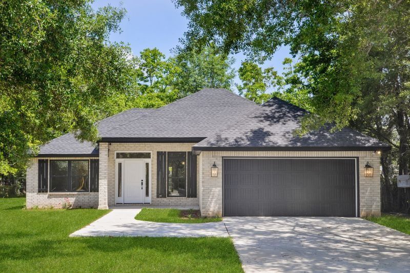 Single-story brick house with a gray roof and a two-car garage, set in a green lawn.