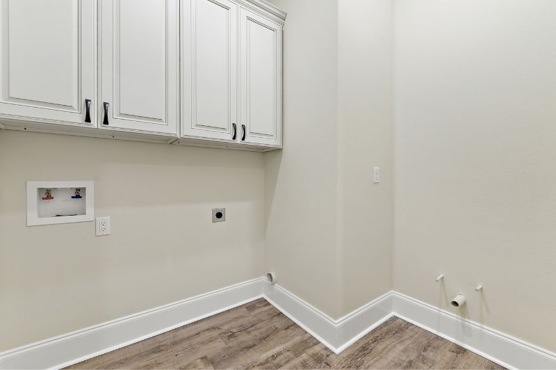 Empty laundry room with white cabinets, a utility box, and light wood-look flooring.