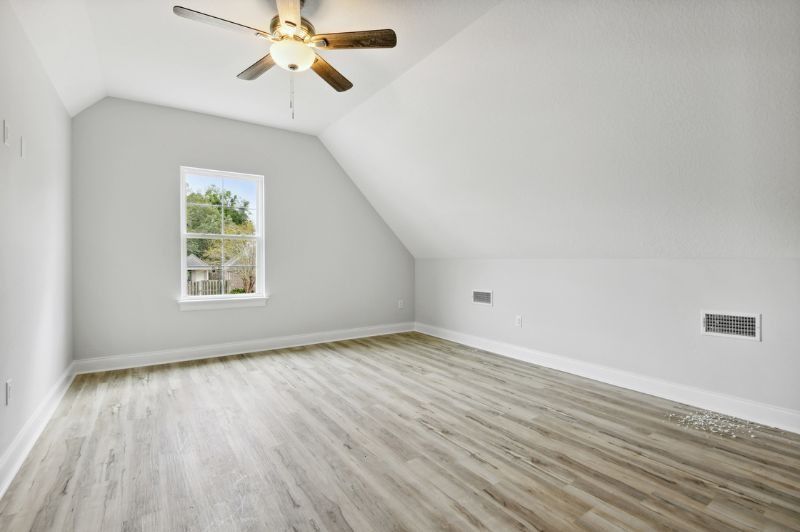 Empty attic bedroom with sloped ceiling, small window, ceiling fan, and wood-look flooring.