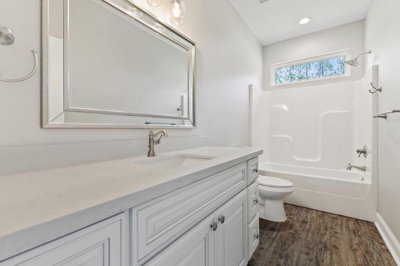 Bathroom with white vanity, mirror, toilet, and bathtub; dark wood-look floor.