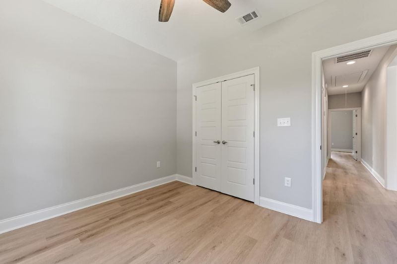 Empty bedroom with gray walls, white trim, closet, and light wood-look flooring.