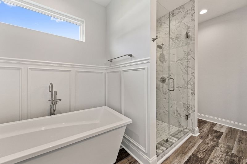 Bathroom with white tub and shower, marble tile, wood-look floor, and window.