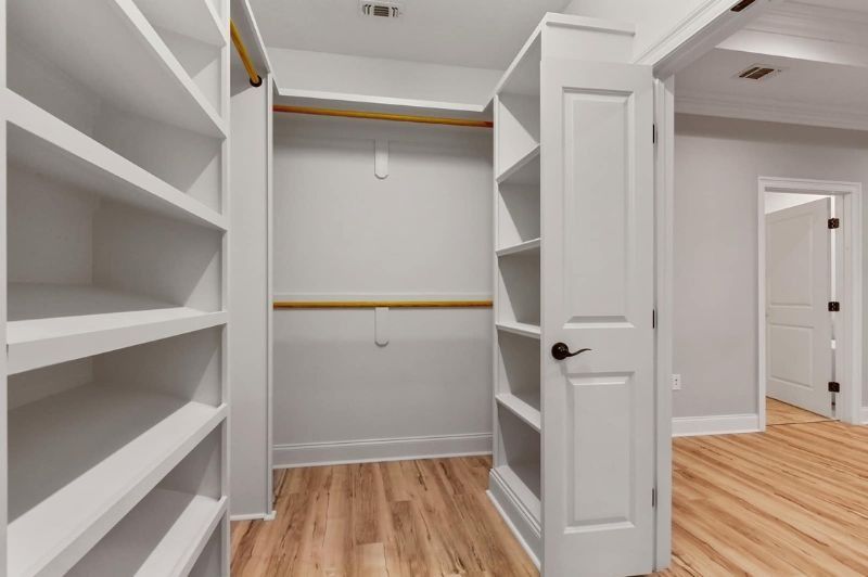 White walk-in closet with built-in shelves and wood flooring; door to hallway on right.