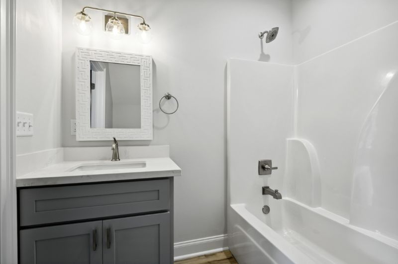Bathroom with gray vanity, white countertop, tub, and shower; white walls, light fixture.