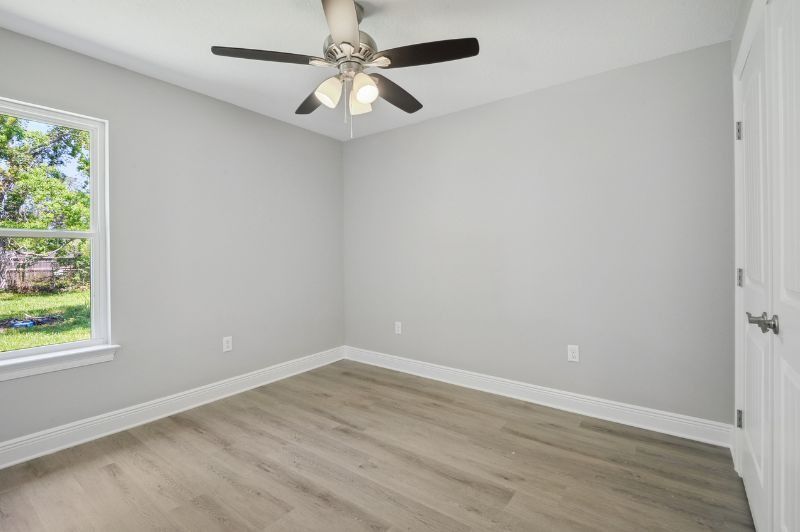 Empty bedroom with gray walls, wood-look floor, ceiling fan, window, and door.