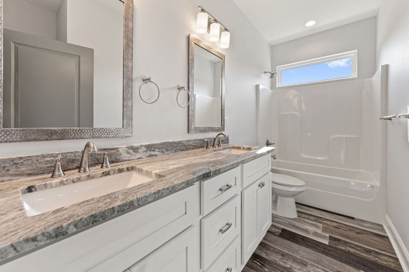 Bathroom with double sink vanity, shower, and toilet; white and gray decor.