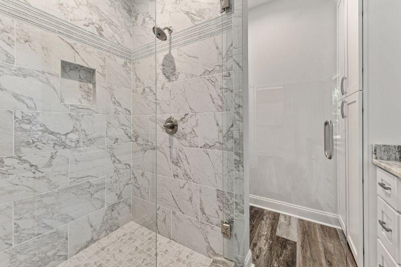 Marble-tiled shower with glass door and silver fixtures. Adjacent white cabinet and wood-look floor.