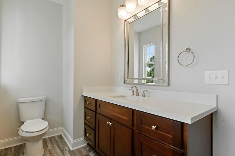 Bathroom with wooden vanity, white countertop, toilet, large mirror, and gray walls.