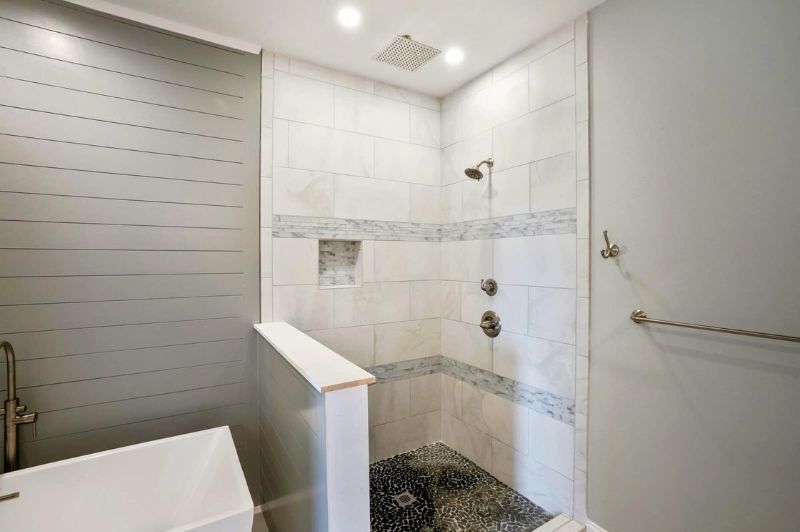 Modern bathroom with a white tiled shower, pebble floor, and blue-gray walls.