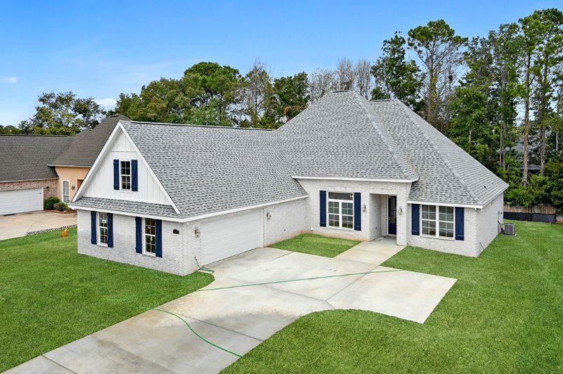 White brick house with grey roof, blue shutters, concrete driveway, green lawn.
