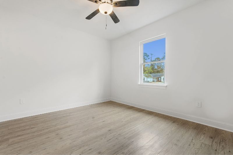 Empty room with white walls, wood-look floor, window, and ceiling fan.