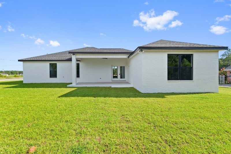 White house with a covered patio and large windows on a grassy lawn under a blue sky.